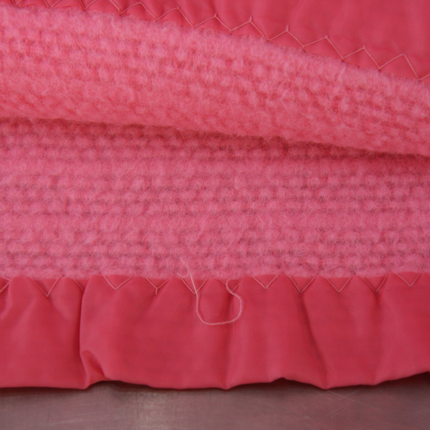Close-up of a pink thermal blanket with nylon binding with pulled stitching