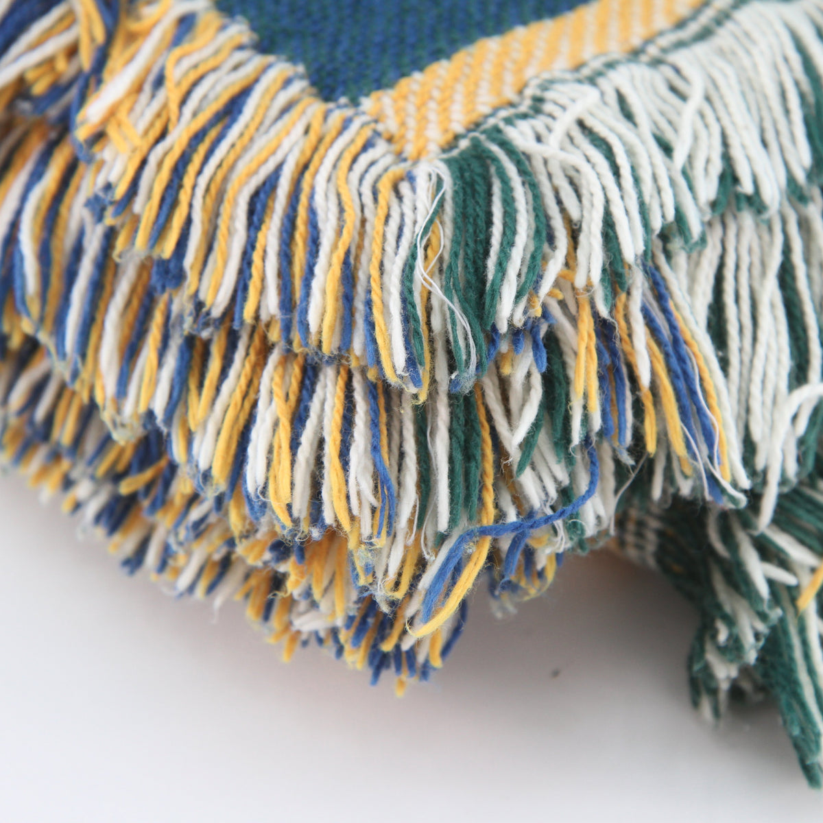 Close-up of a woven throw blanket corner with multicolored fringe in blue, yellow, and white, and a blue and yellow patterned woven section.